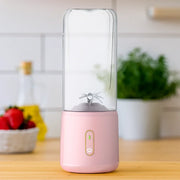 Pink protein shaker bottle with transparent Tritan body and built-in mixing blades on wooden kitchen countertop.